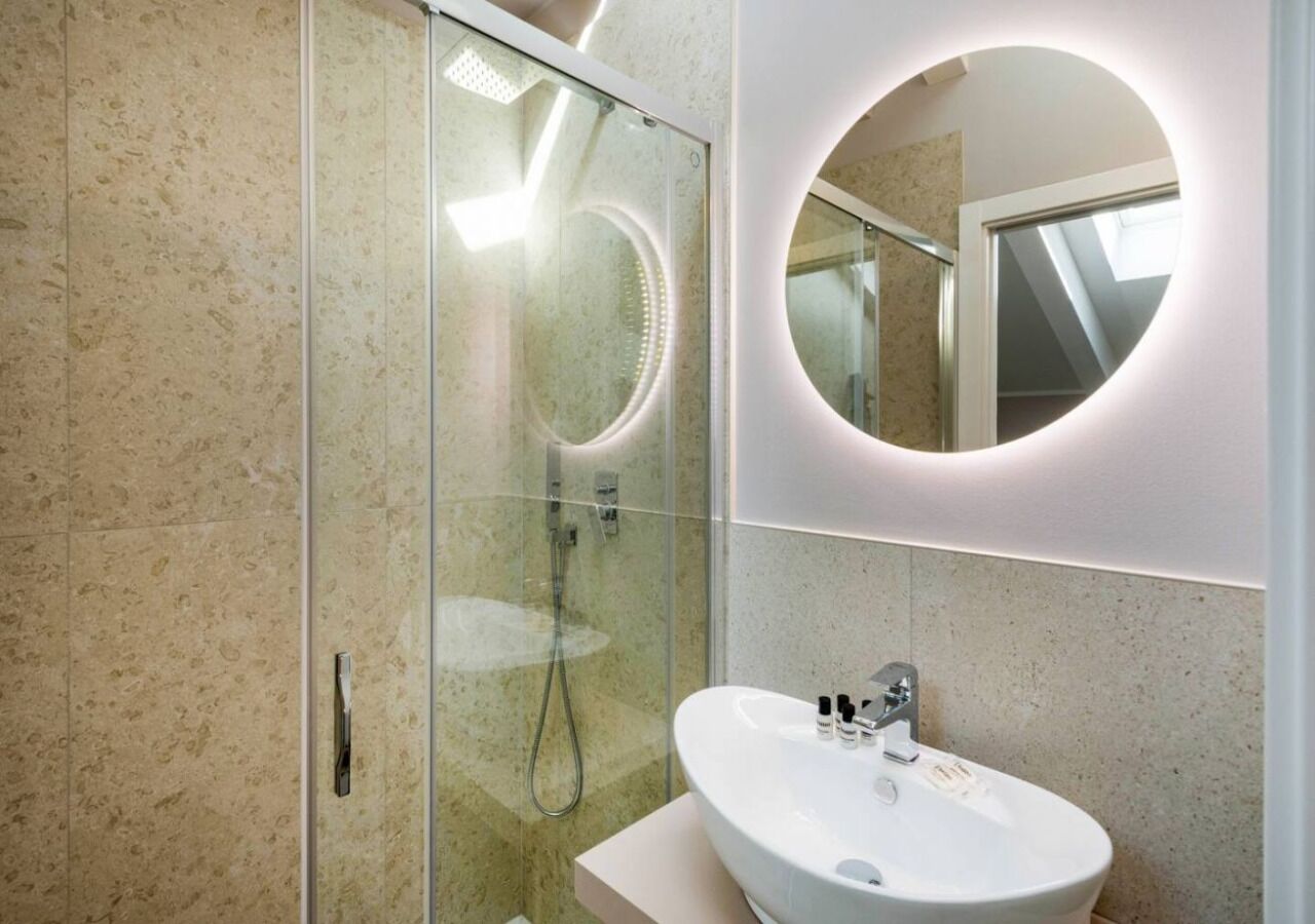 A modern bathroom with a glass shower enclosure, a round mirror, and a white sink.