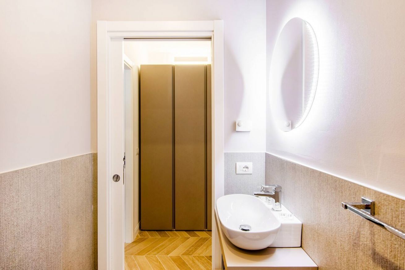 A compact bathroom with a white sink, a mirror, and a door leading to a toilet.