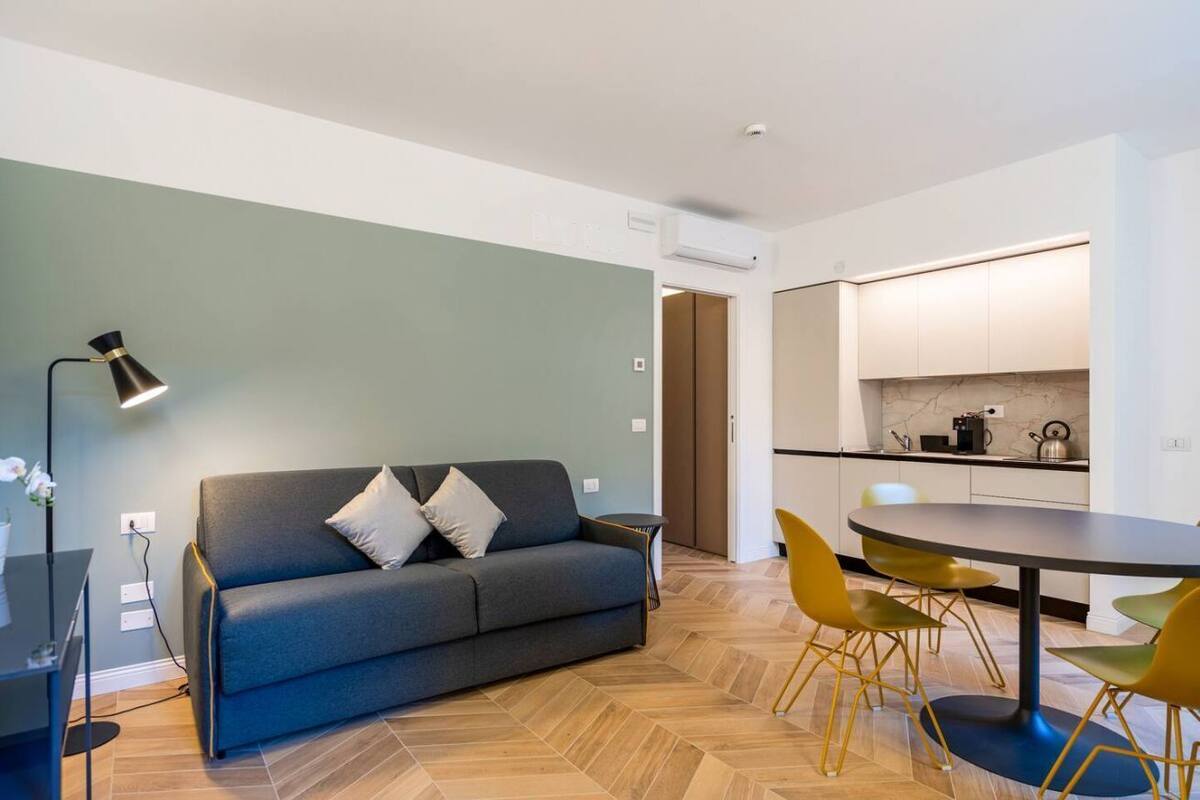 A modern living room with a sofa, a dining table with chairs, and a lamp.