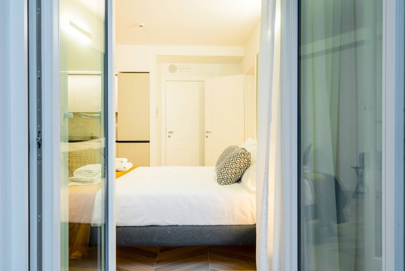 A hotel room with a bed, a small table with towels, and a door.