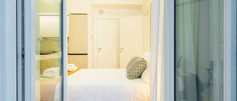 A hotel room with a bed, a small table with towels, and a door.