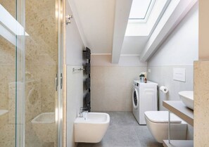 A compact, modern bathroom with a glass shower enclosure, a built-in washing machine, and a toilet. - JOIVY Premium Apartments Trieste Mazzini (Trieste)
