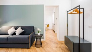 A modern living room with a sofa, a small side table, and a mirror with a wooden hanger. - JOIVY Premium Apartments Trieste Mazzini (Trieste)