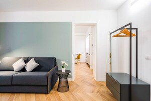 Un soggiorno moderno con un divano, un piccolo tavolino e uno specchio con un appendiabiti in legno.