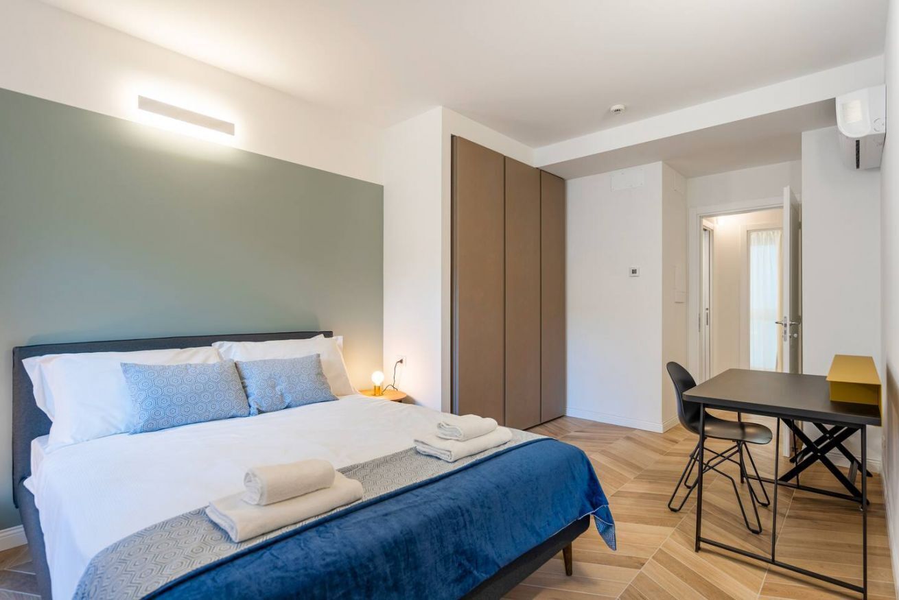 A modern bedroom with a bed, bedside table, and a desk with a chair.