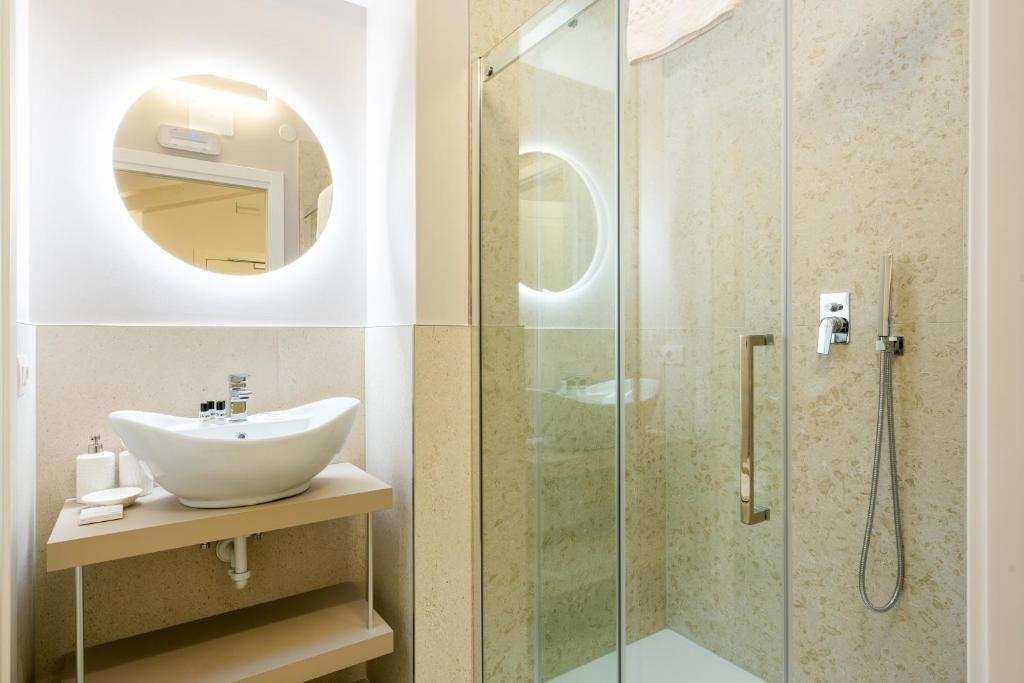 Uma casa de banho moderna com cabine de duche em vidro, espelho redondo e lavatório suspenso branco.