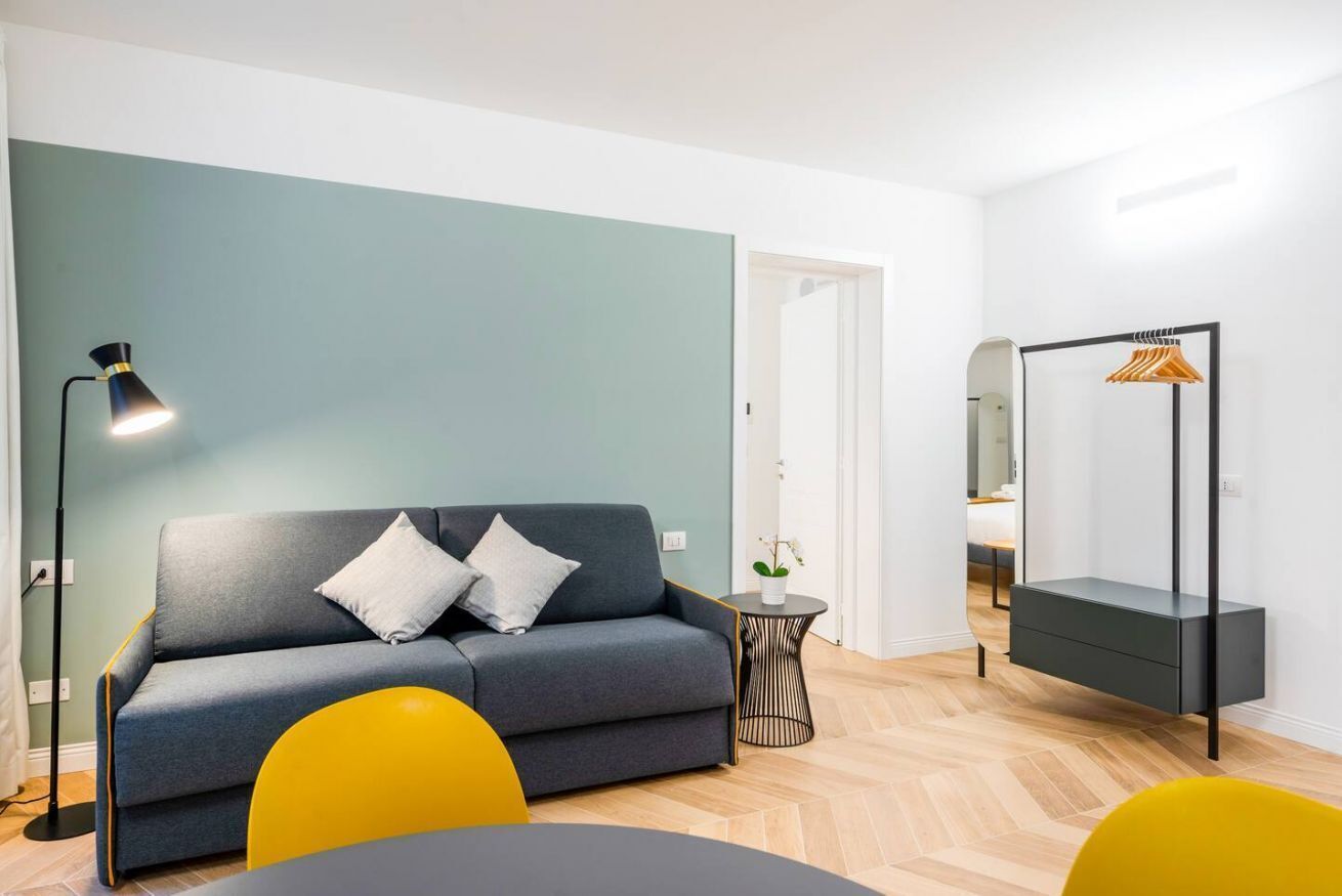 A modern living room with a grey sofa, yellow chairs, a black floor lamp, and a hanging wardrobe.