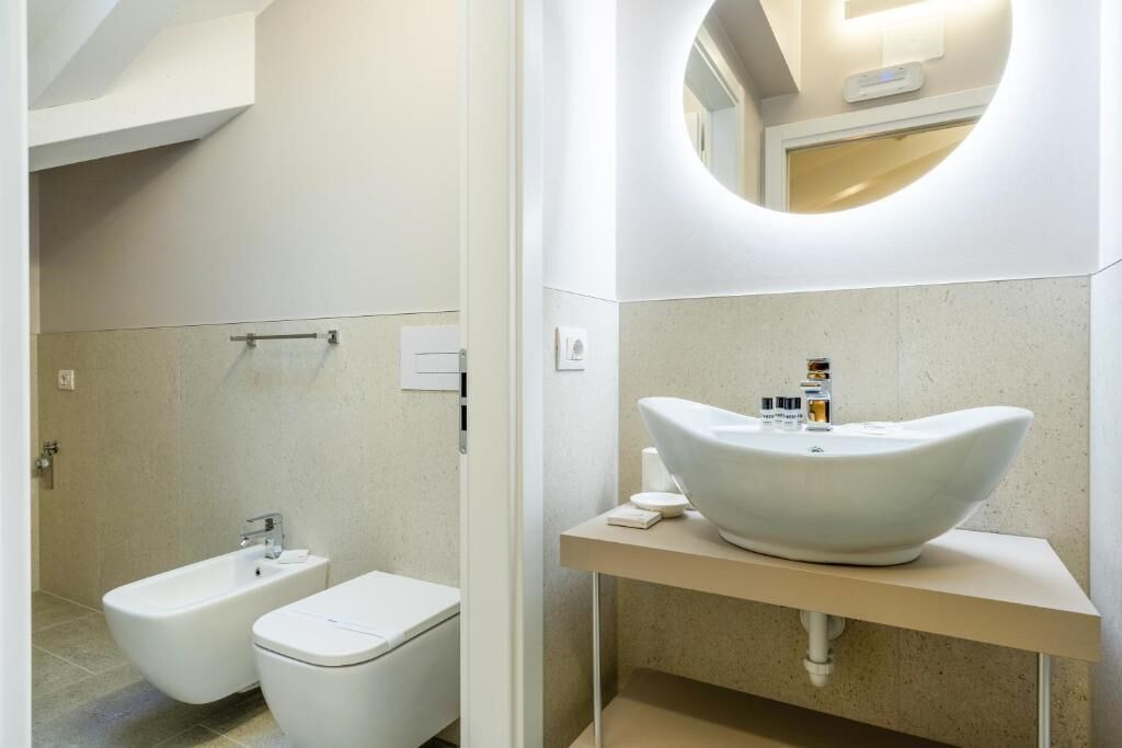 Un baño moderno con un lavabo independiente, un inodoro y un amplio lavamanos ovalado con un espejo superior.
