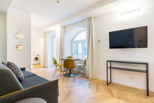 Un soggiorno moderno con un divano, un tavolo da pranzo con sedie, una TV a parete e un pavimento con motivo a spina di pesce.