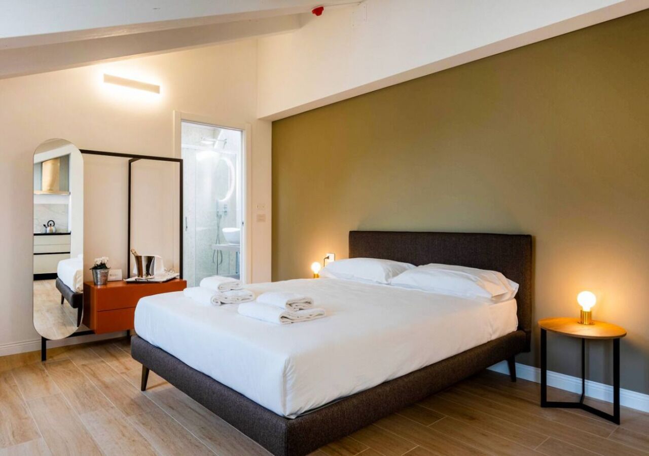 Une chambre d’hôtel moderne, dotée d’un grand lit, de tables de chevet, d’une armoire et d’une salle de bain visible à travers une porte ouverte.