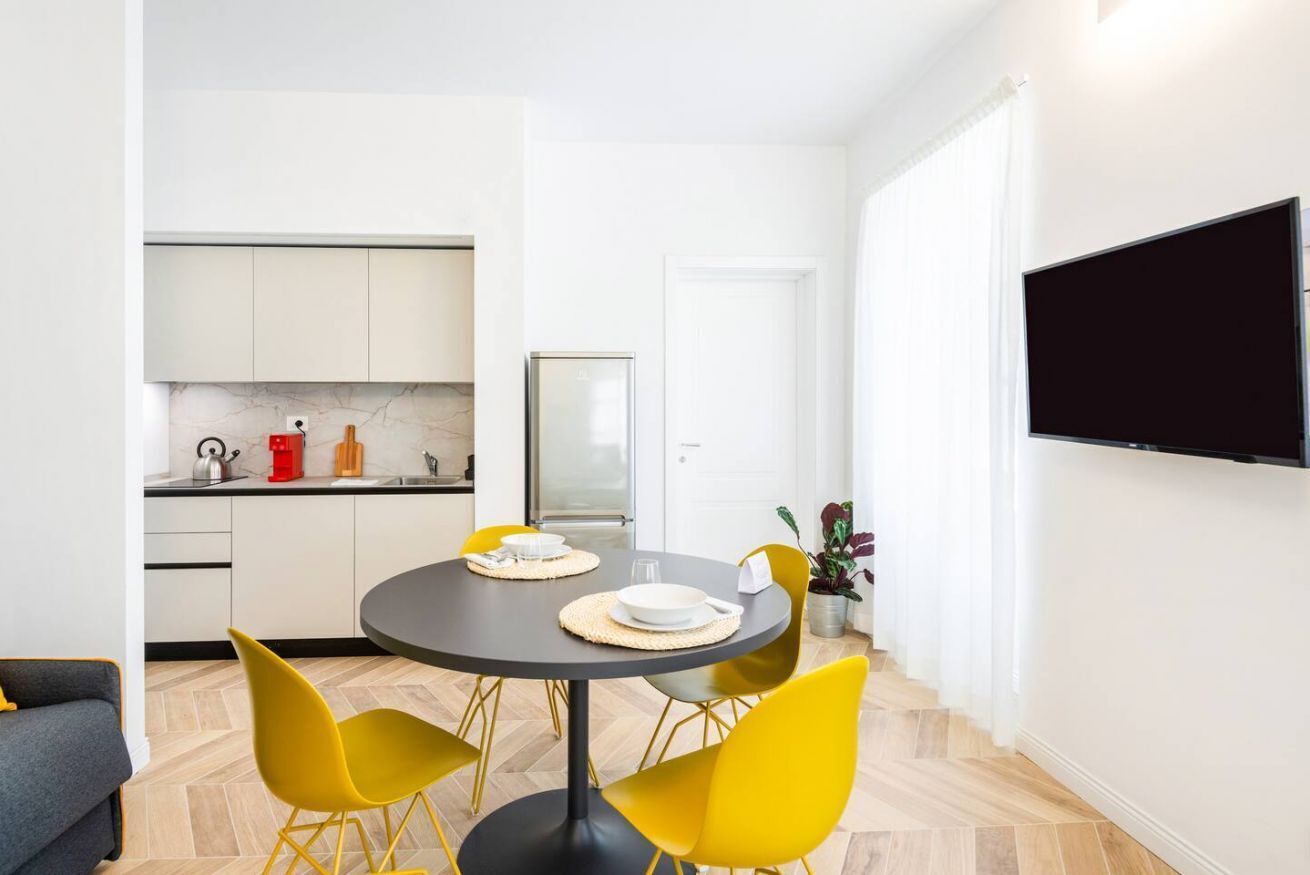 A compact living space with a dining area, kitchenette, and a flat-screen TV mounted on the wall.
