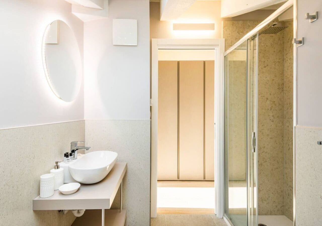 A modern bathroom with a large oval mirror, a white sink, and a glass shower enclosure.