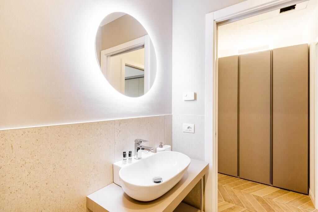 A modern bathroom with a round mirror, a white sink, and a wooden floor.