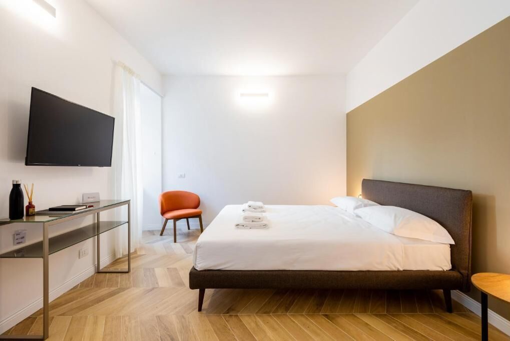 A modern hotel room with a bed, a desk, a chair, and a flat-screen TV.