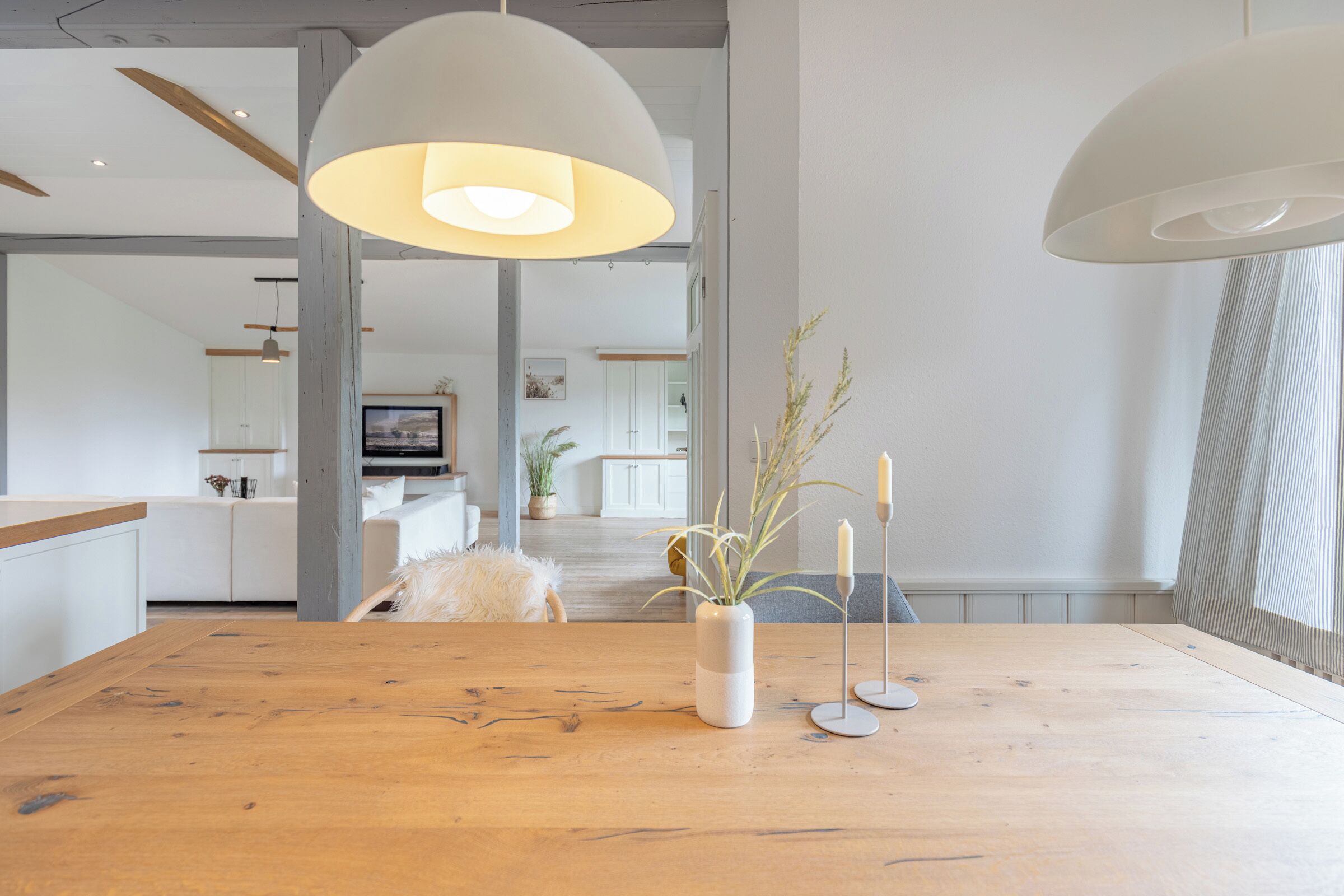 Ein modernes Interieur mit einem Holztisch, weißen Pendelleuchten und einer Pflanzvase.