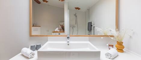 A modern bathroom with a large mirror, white sink, and a skylight above.