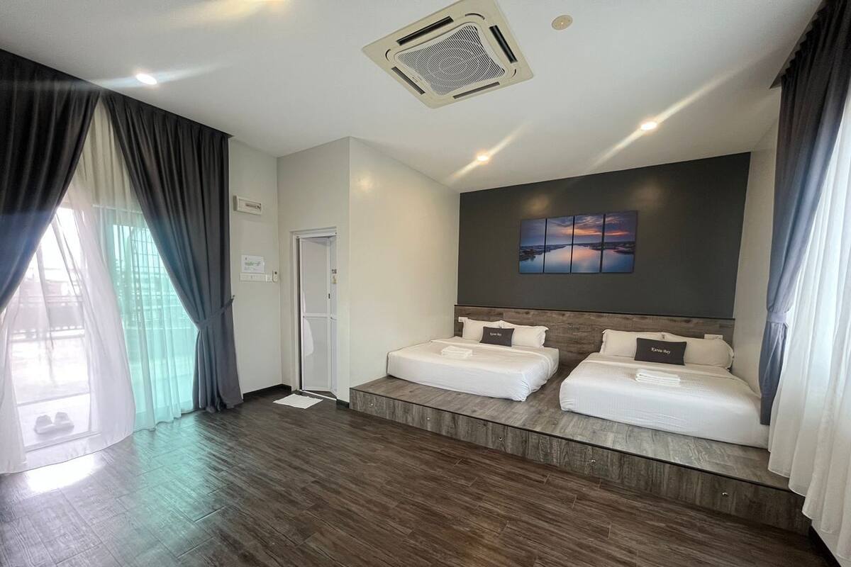 Quarto de hotel com uma cama grande, uma mesinha e uma janela com cortinas.