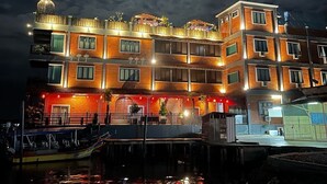 Un edificio de varios pisos con un tanque de agua en la azotea, varios balcones y un muelle con barcos.