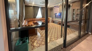 Habitación de hotel con un separador de vidrio, un sofá de cuero marrón, una mesa de centro, un televisor y un suelo con estampado.