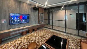 Un vestíbulo moderno con un televisor de pantalla plana grande, una zona de estar con un tapiz estampado y un separador de vidrio.