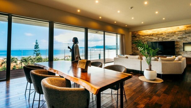A modern living room with a large wooden table, comfortable seating, a flat-screen TV, and a stone wall. - A special retreat in Ishigaki Island｜Private villa exclusively for one group per day (ishigaki city)