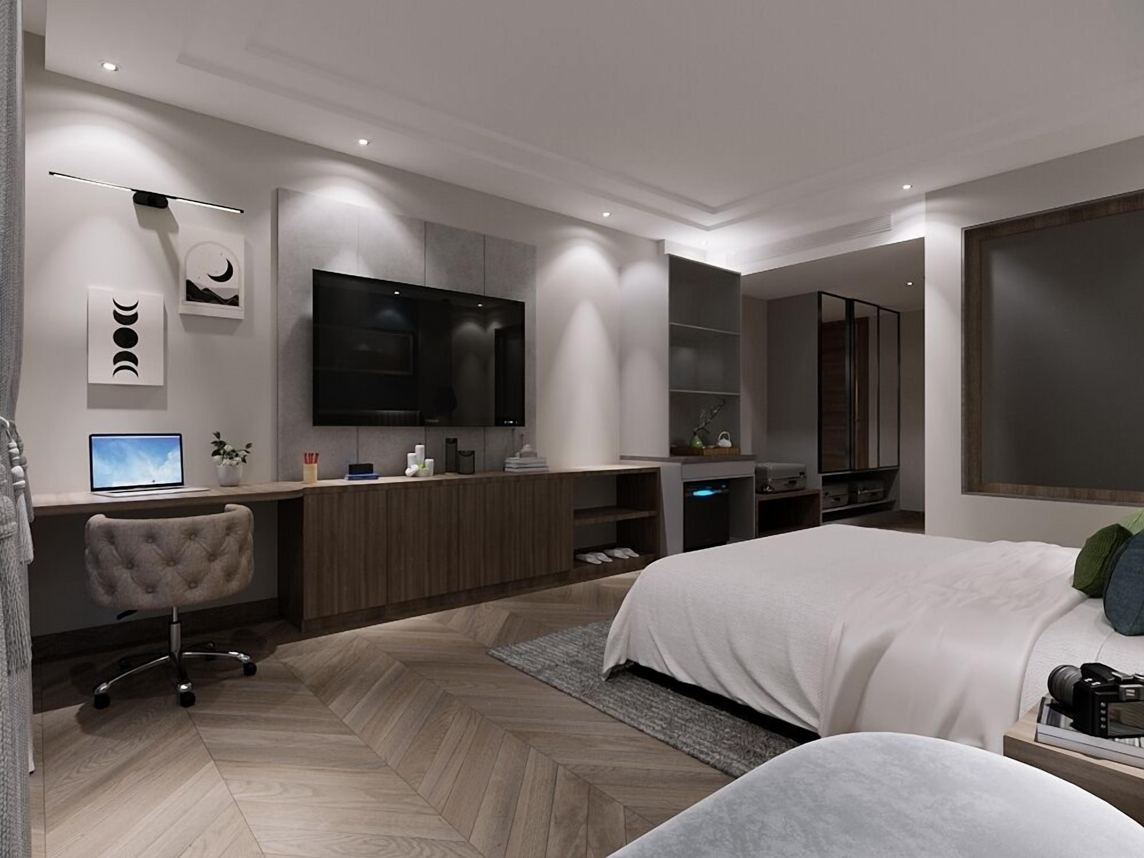 Un dormitorio moderno con una cama grande, un escritorio con computadora, un televisor y un espejo.