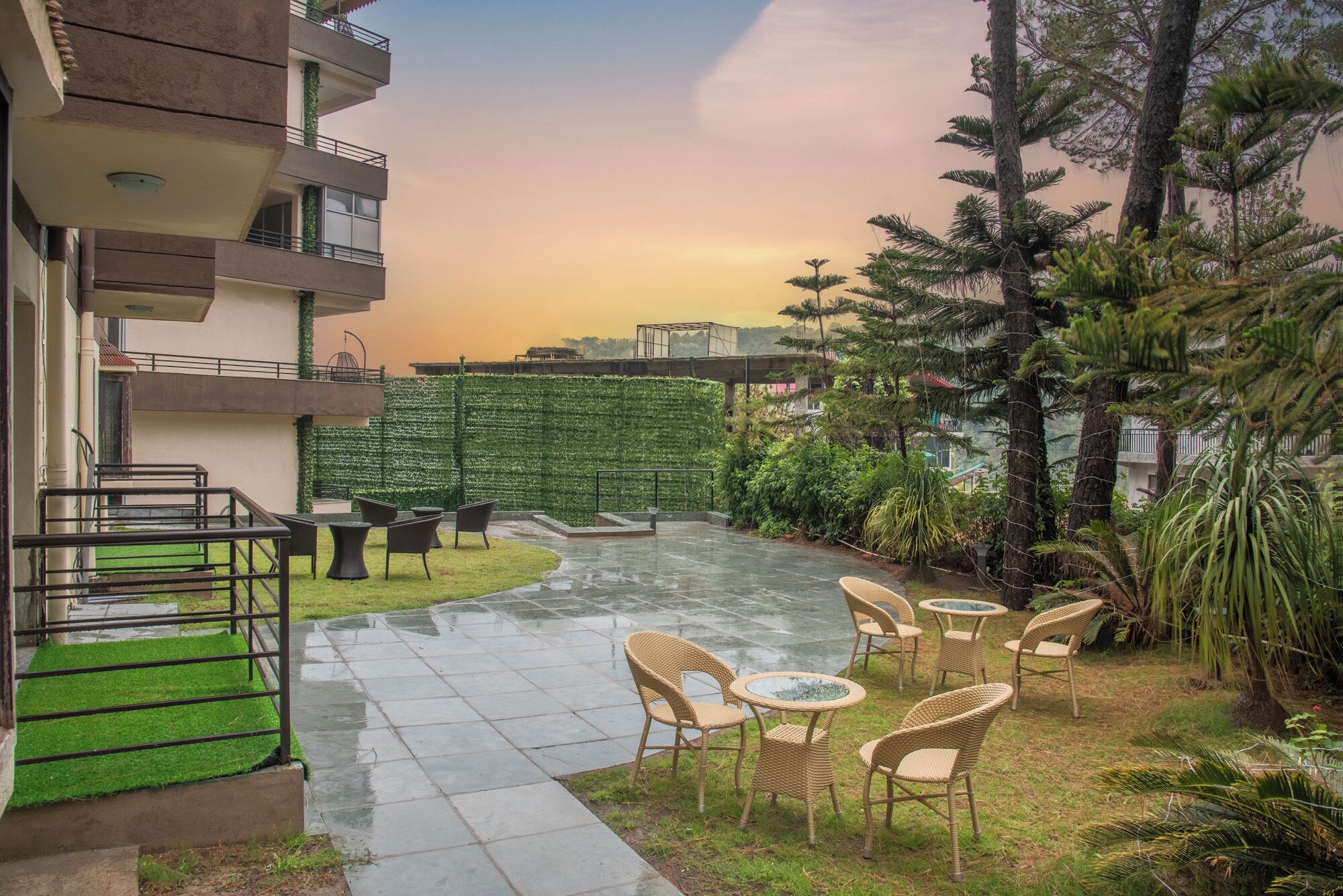 A courtyard with outdoor seating, a green wall, and tall trees.