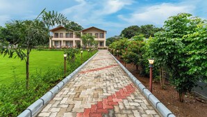 A pathway leading to a building with a garden and trees. - Milestone Resort (Udaipur)