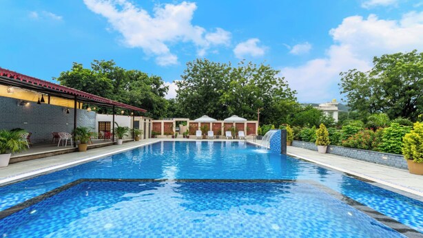 A swimming pool with tiled flooring, surrounded by potted plants and outdoor seating. - Milestone Resort (Udaipur)