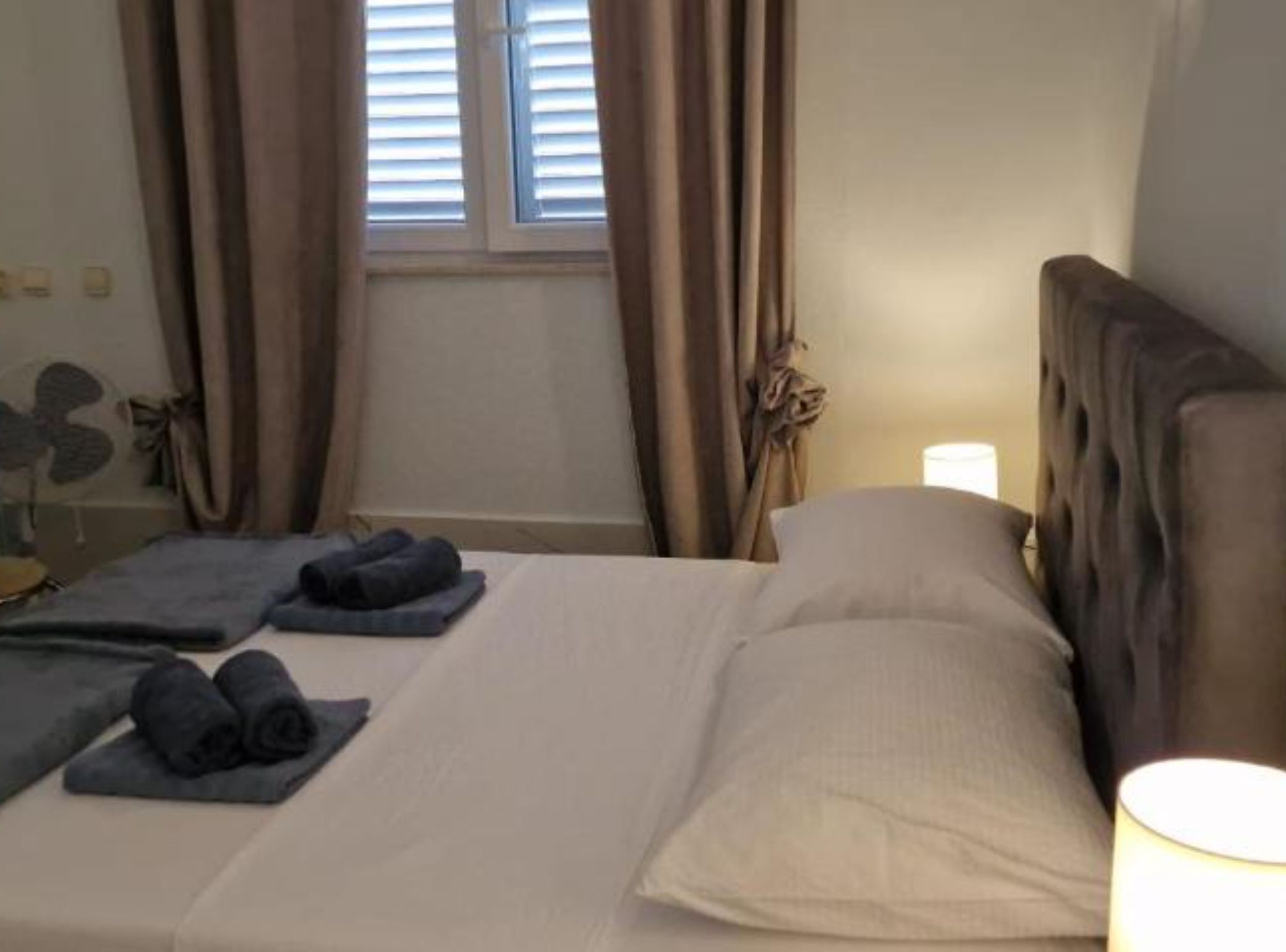 A neatly made bed with pillows and folded towels, a bedside lamp, and a window with curtains.