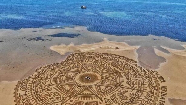 Une plage où l’on peut admirer, au premier plan, un grand et complexe motif de mandala réalisé dans le sable.