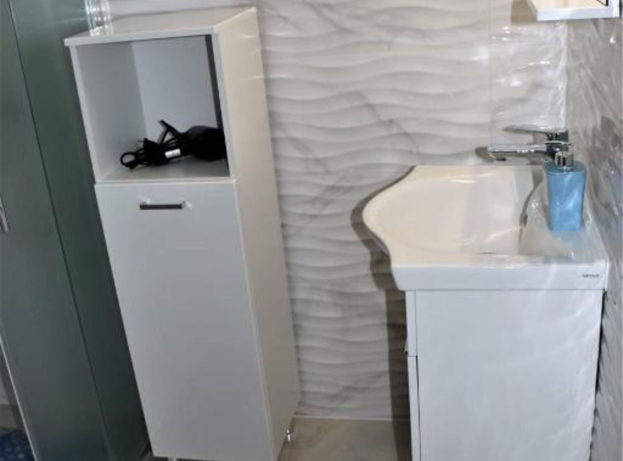 Une salle de bain avec un lavabo blanc, un miroir au-dessus et un meuble blanc doté d’une petite étagère.