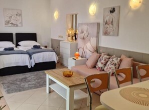 Un dormitorio con dos camas, una mesita de noche con lámpara, un sofá con cojines y una mesa de comedor con sillas.