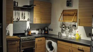 A modern kitchen with wooden cabinets, stainless steel appliances, and a built-in washing machine. - 2-bed Seaside Apartment - Sleeps 5 & Free Parking (Edinburgh)
