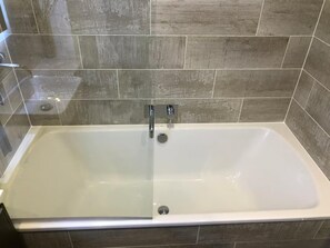 A modern bathroom with a rectangular bathtub, tiled walls, and a visible showerhead. - 2-bed Seaside Apartment - Sleeps 5 & Free Parking (Edinburgh)