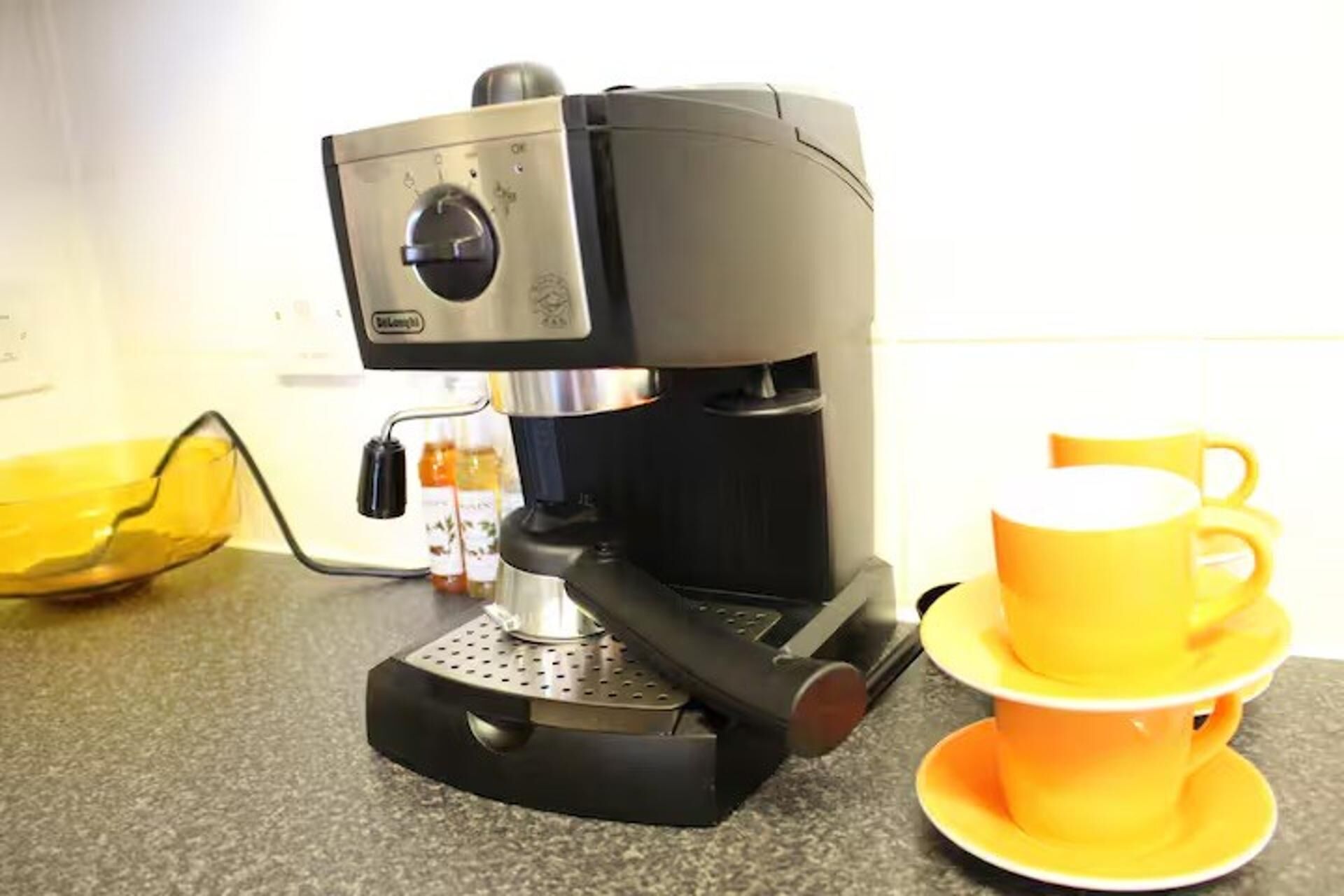 A coffee maker with a control panel and a yellow cup and saucer on a countertop.