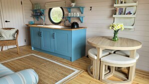 A cozy kitchen with blue cabinets, a round wooden table, and a wicker chair. - Cabins in Oxfordshire with Hot Tub & Meadow Views (Banbury)