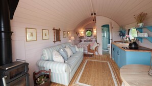 A cozy interior with a striped sofa, a wooden chair, a kitchen area, and a fireplace. - Cabins in Oxfordshire with Hot Tub & Meadow Views (Banbury)