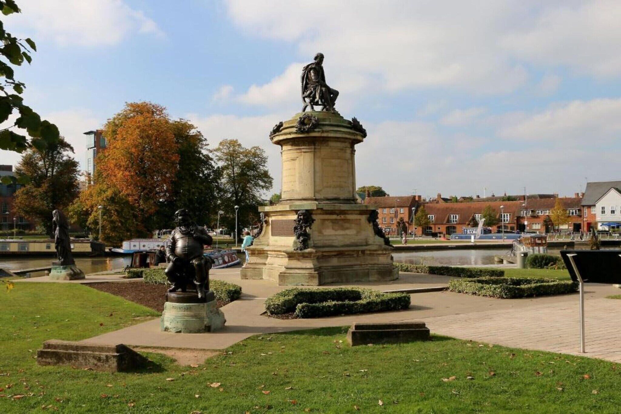 A public square with a central monument, a fountain, and surrounding greenery.
