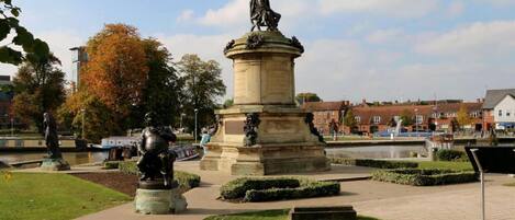 A public square with a central monument, a fountain, and surrounding greenery.