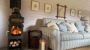 A cozy room with a wood-burning stove, a striped sofa, and framed pictures on the wall. - Cabins in Oxfordshire with Hot Tub & Meadow Views (Banbury)