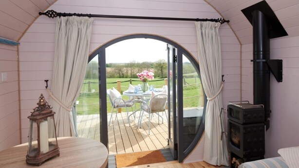 A cozy room with a wooden deck, a fireplace, and a table with chairs. - Cabins in Oxfordshire with Hot Tub & Meadow Views (Banbury)