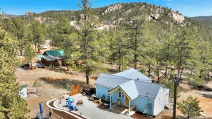 A lodge with a blue exterior, surrounded by trees and a rocky mountain backdrop.