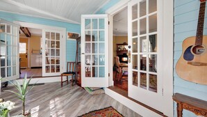 A room with wooden floors, a guitar, and a door leading to another room.