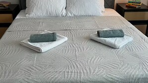 Un lit bien fait, recouvert d’une courtepointe matelassée, avec deux serviettes enroulées et une pile de livres sur une table de chevet.