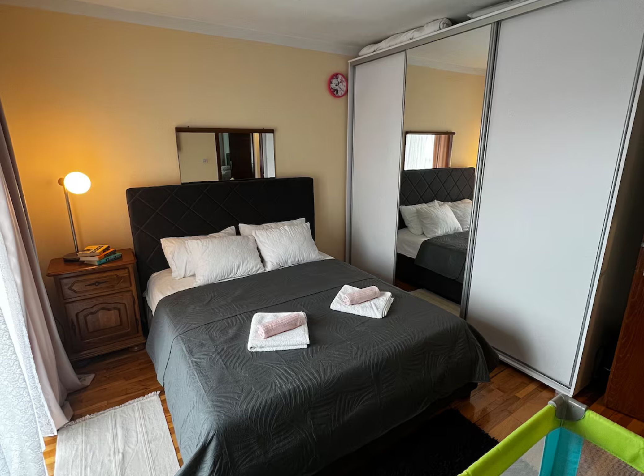 Un dormitorio con una cama grande, una mesita de noche con lámpara, un espejo y un armario.