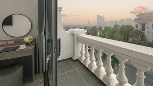 A balcony with a view of a cityscape, a round mirror, and a desk with a laptop and a cup.