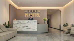 A hotel reception area with a marble reception desk, a receptionist, and a wall displaying clocks and city names.