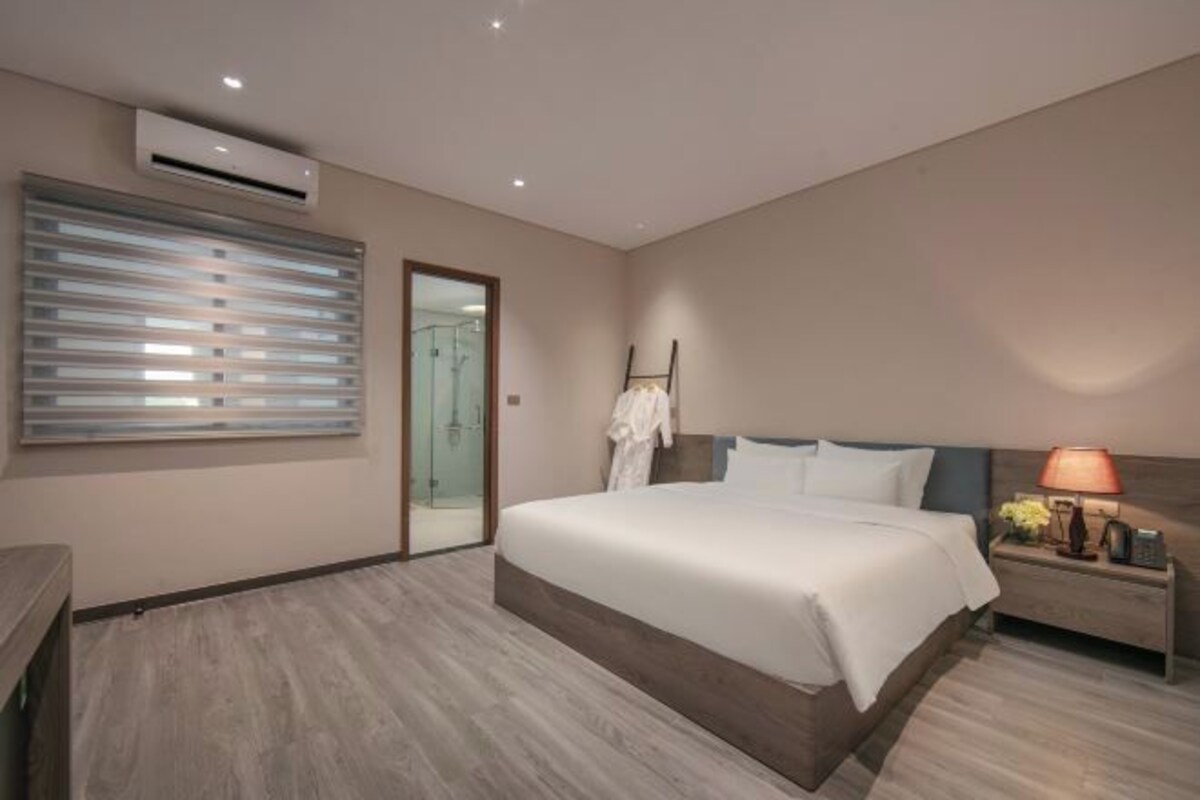 Een moderne hotelkamer met een groot bed, een nachtkastje met een lamp en een glazen schuifdeur naar een douche.