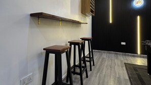 Eine moderne Bar mit drei Hockern, einer Holzablage und einer Wand in Schwarz mit vertikaler Beleuchtung.
